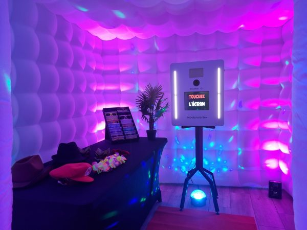 Une borne photo dans un igloo illuminé par des spots lumineux. À côté nous avons une table qui contient des accessoires (lunettes, chapeaux) pour faire des photos souvenirs amusantes.