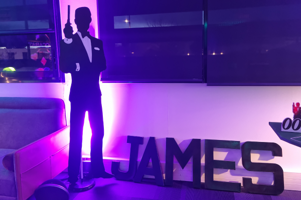 Une silhouette James Bond avec un spot lumineux qui éclaire le fond. À côté se situe les lettres 
