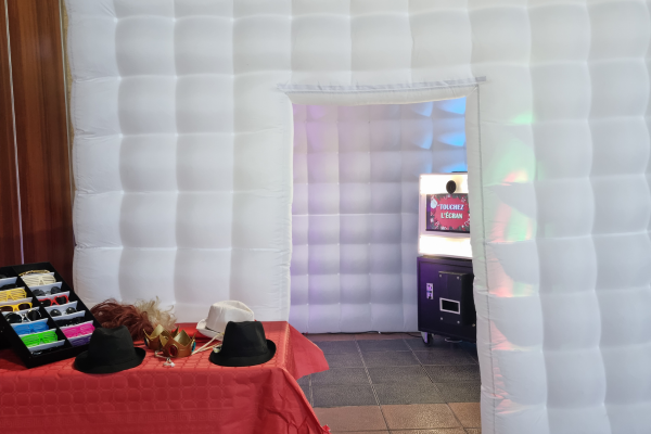 Un igloo gonflable qui fait office d'espace pour se prendre en photo avec la machine borne photo qui se situe à l'intérieur. En premier plan, une table avec une nappe rouge où reposent des accessoires (lunettes, chapeaux, perruques), pour faire des photos amusantes.