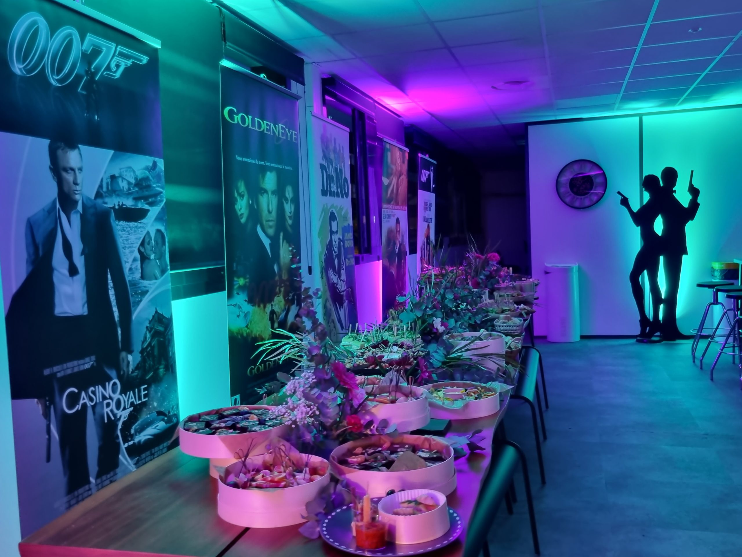 décoration sur le thème James Bond, avec des affiches de films, une silhouette, des spots qui illuminent la salle, et de la nourriture sur la table.